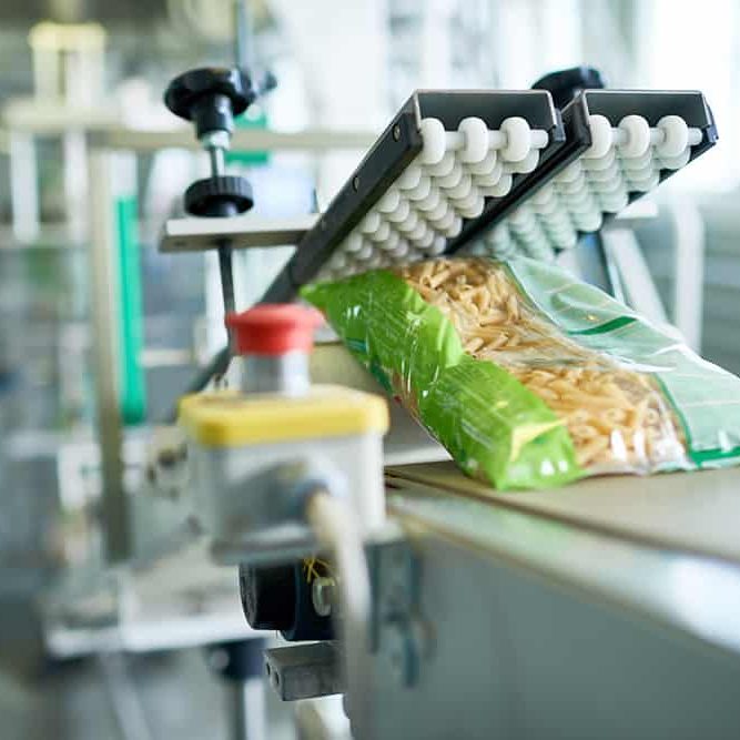 Close up of production process at modern food factory, focus on macaroni bag ready for packaging sliding down assembly line, copy space